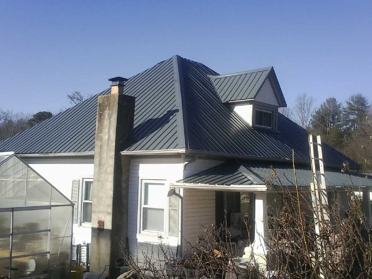 Dark blue standing seam metal roof on a white farmhouse with dormer — Slate & Tile Roof Repair by Roofing Brothers in Batchelor
