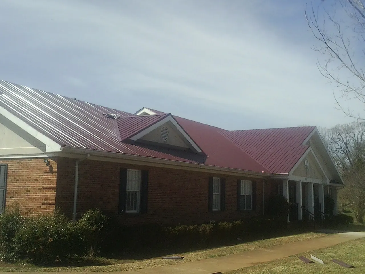 Red metal roof with gabled entries on a long brick building, from a Hail Damage Roof Repair job in Batchelor