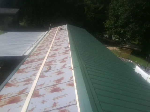 Old rusted panels beside newly installed green metal roofing — Wind Damage Roof Repair by Roofing Brothers in Batchelor