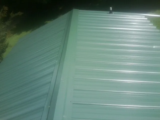 New green metal panels meeting at the ridge of a roof — Flat Roof Repair work by our crew in Batchelor