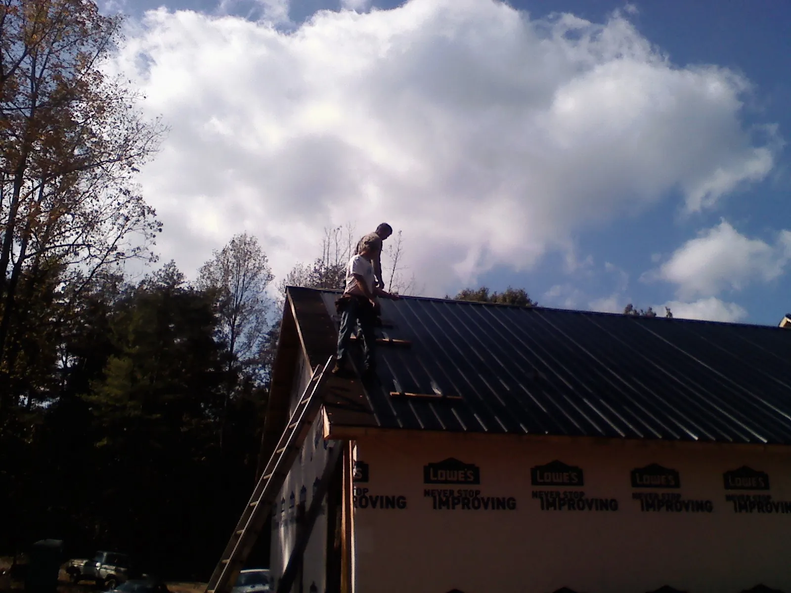 Roofer fastening dark metal panels high against a cloudy sky, from a Roof Inspection job in Batchelor