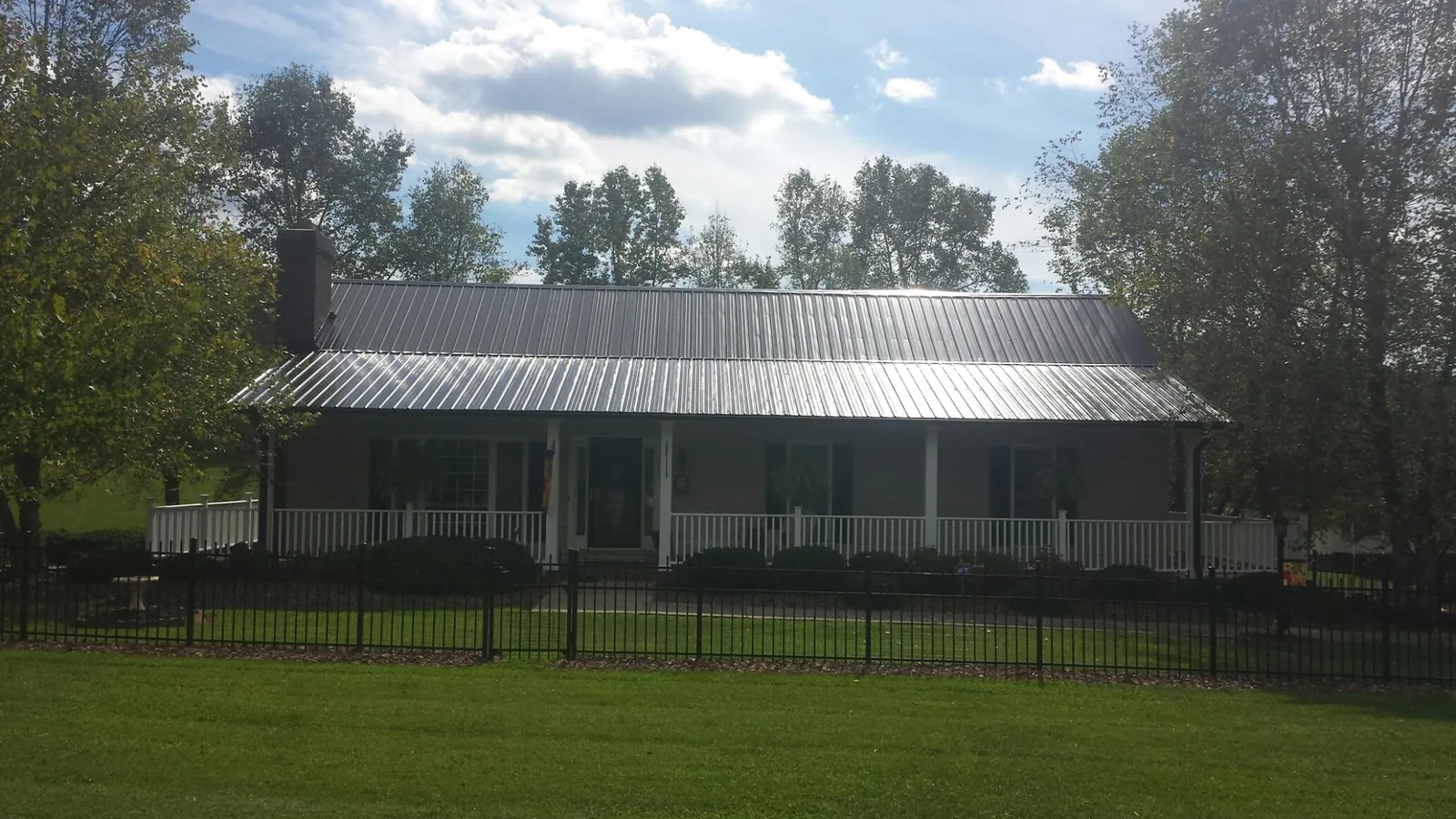 Gray metal roof on a brick ranch with a full width front porch — Gutter Guard Installation work by our crew in Batchelor