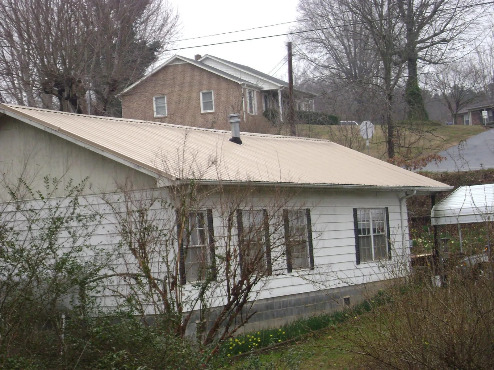 Tan metal roof on a white sided house set into a hillside — Commercial Roofing by Roofing Brothers in Batchelor